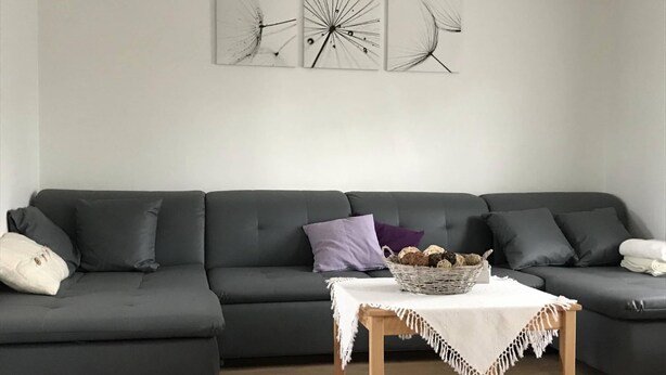 A modern living room with a dark grey sectional sofa, a small wooden table with a basket, and three abstract wall art pieces. - Countryside Stay With Terrace (Heers)