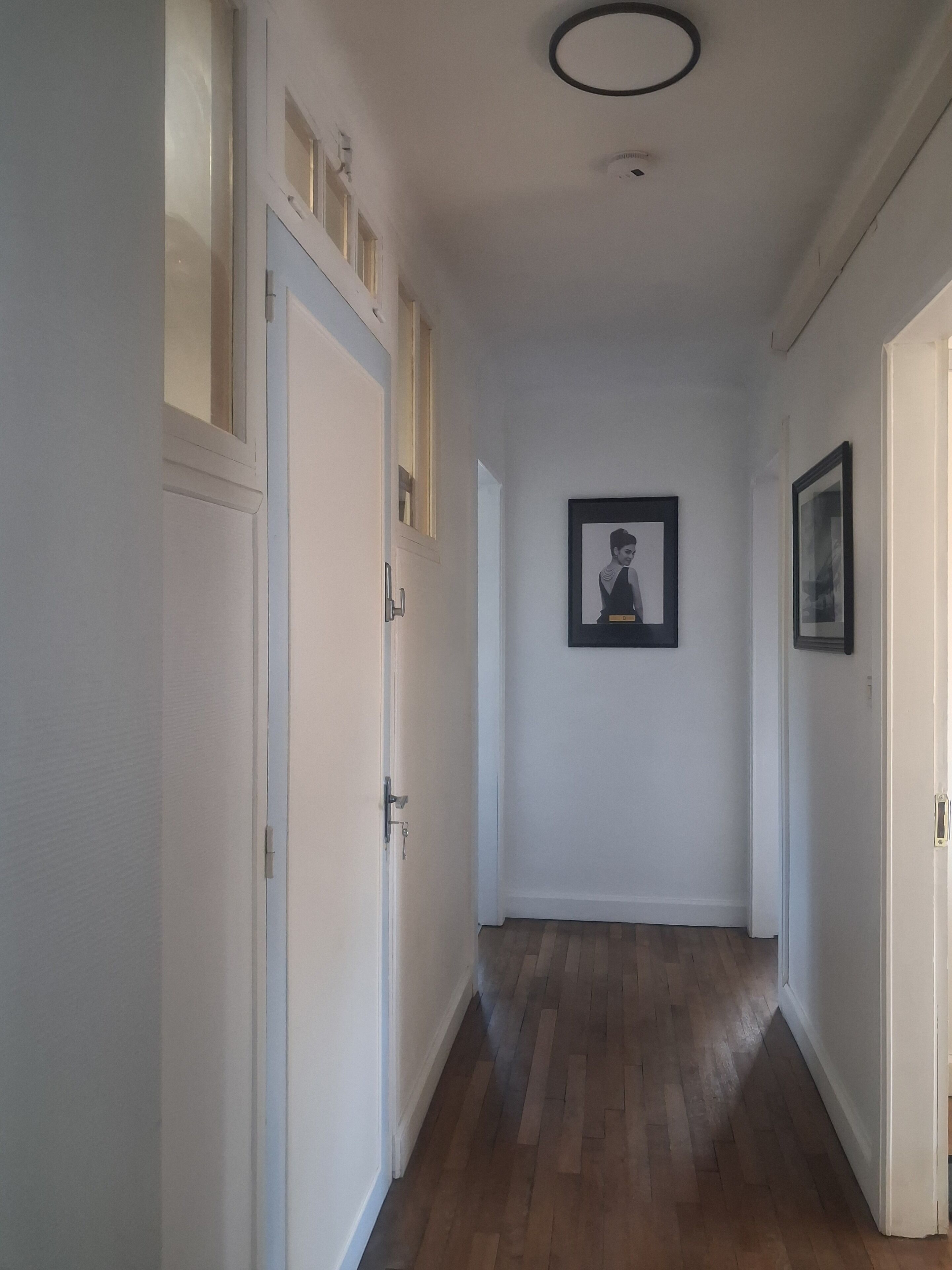 Een gang met houten vloer, witte wanden en deuren aan beide zijden. Er hangt een lijst met een afbeelding aan de muur.