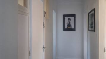Een gang met houten vloer, witte wanden en deuren aan beide zijden. Er hangt een lijst met een afbeelding aan de muur.