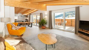 A modern living room with a sofa, TV, and a dining area with a table and chairs. - Experience beautiful high-ceilinged living rooms with exposed roof trusses! (Wildschönau)