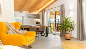 A modern living room with a bright yellow sofa, a dining area with a wooden table, and a kitchen with a stove. - Experience beautiful high-ceilinged living rooms with exposed roof trusses! (Wildschönau)