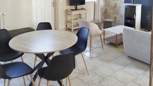 Una habitació amb una taula rodona de fusta, cadiretes negres i blanques, una televisió sobre un moble, una llar de foc i una paret amb paper pintat.