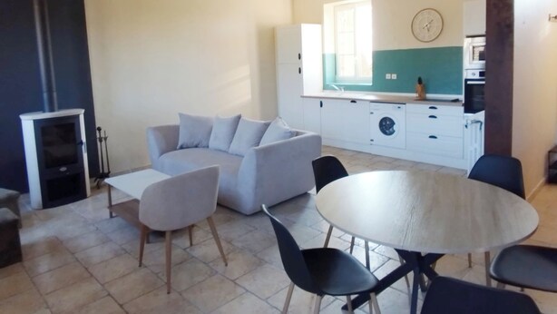 Un saló amb un sofà, taula de dinar, cadires, zona de cuina amb un rentaplat i una finestra.