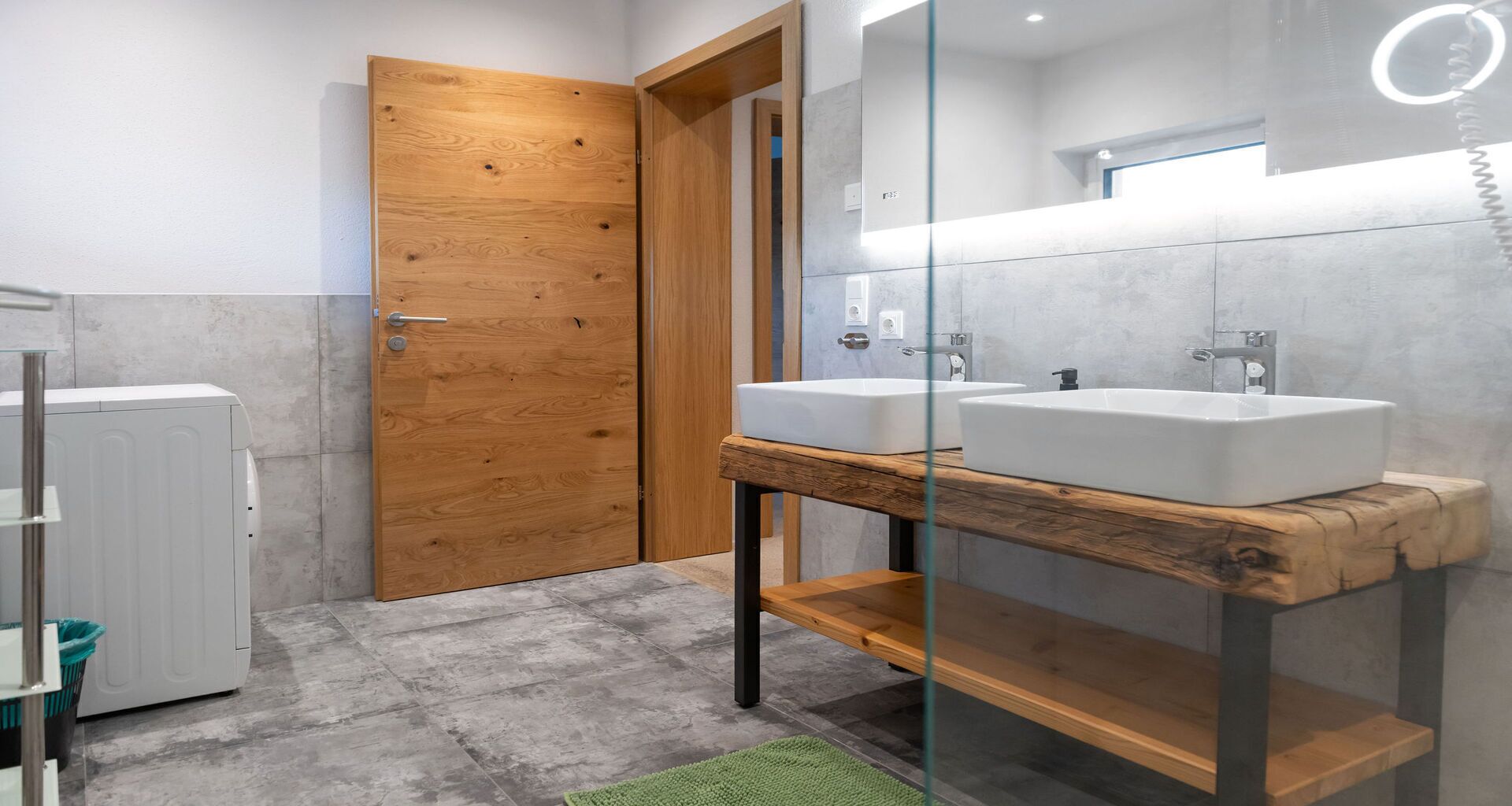 Une salle de bain avec deux lavabos, une porte en bois et une cabine de douche en verre.