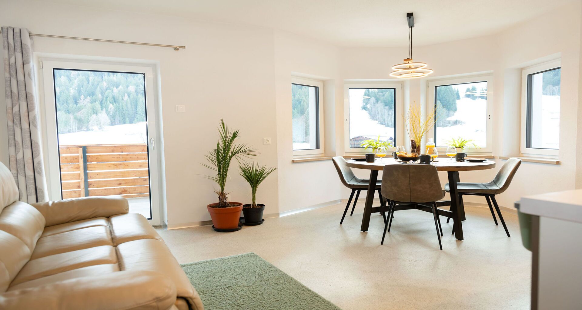 En moderne stue med sofa, spiseområde med bord og stole, plantepotteskjulere og store vinduer.