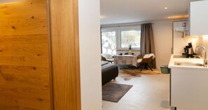 Une chambre d’hôtel moderne avec une porte en bois, un canapé, une table à manger avec des chaises, un coin cuisine et une vue par la fenêtre.