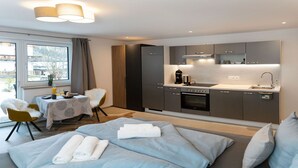 Une chambre d’hôtel moderne équipée d’un lit, d’une table à manger, d’une chaise et d’un coin cuisine avec une cuisinière, un four et un évier.