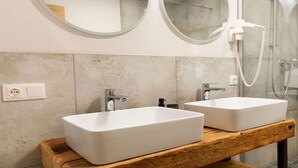 Een badkamer met twee witte wasbakken, een houten wastafelmeubel, een spiegel en een douche.