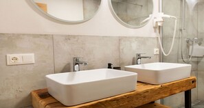 Ein Badezimmer mit zwei weißen Waschbecken, einer Holz-Kommode, einem Spiegel und einer Dusche.