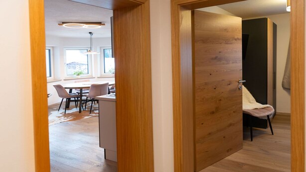 Een modern interieur met een houten deur, een eethoek met stoelen en een tafel, en uitzicht op het buitenlands gebied.