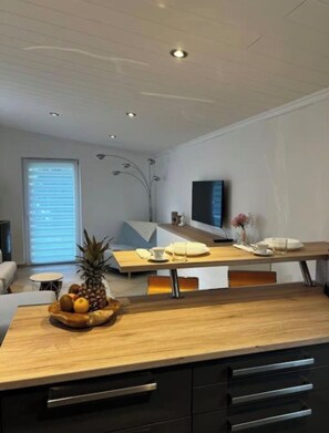 A modern kitchen with a wooden countertop, black cabinets, and a dining area with a table set for two. - Garden Apartment Ammersee (Herrsching am Ammersee)
