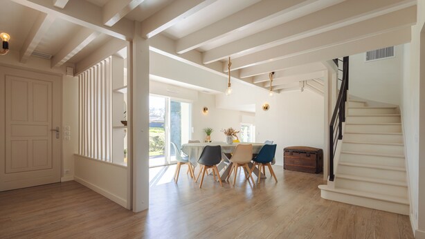 A spacious room with wooden flooring, a dining area with chairs and a table, a staircase, and a large window. - Villa Solanne - Garden, pool & comfort / 10 travellers (Narrosse)