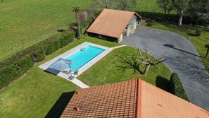 A residential property with a swimming pool, a patio with outdoor furniture, and a detached house with a tiled roof.