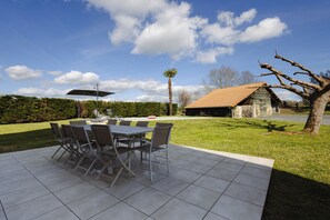 An outdoor patio with a table and chairs, a palm tree, and a stone building in the background.