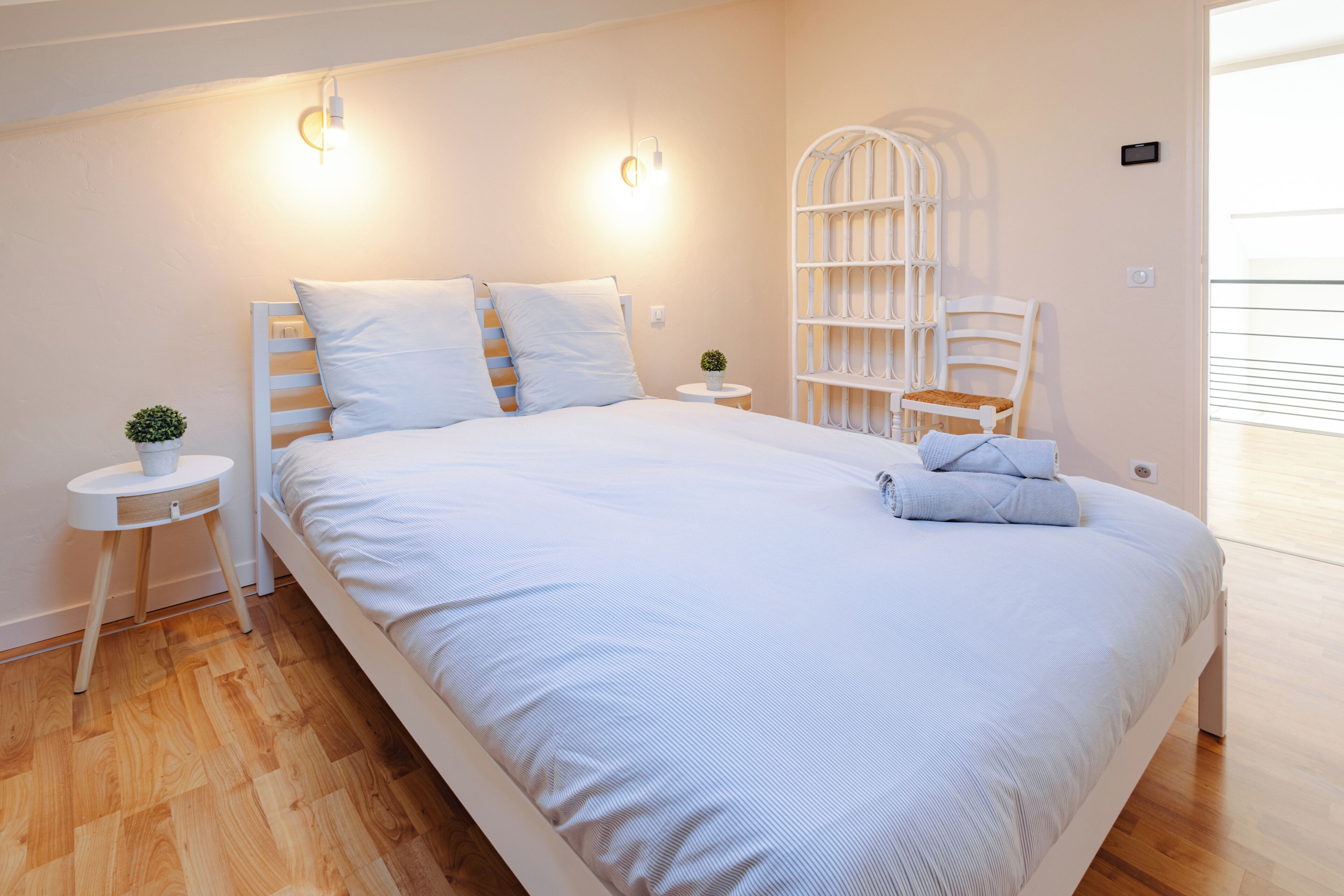 Un dormitorio con una cama grande, mesitas de noche, una planta pequeña y una silla blanca.