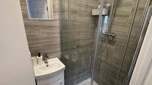 Een badkamer met een douche met glazen wanden, een witte wastafel en een spiegel boven de wastafel.
