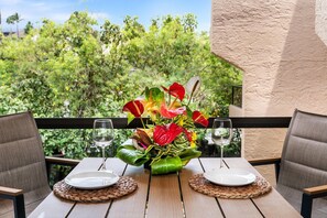 Ein Tisch ist gedeckt mit Tellern, Weingläsern und einer Blumenarragemant auf einem Balkon mit Blick auf Grünflächen.