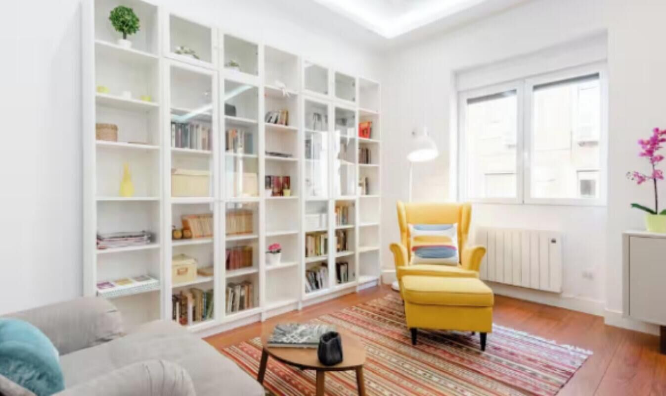 Un soggiorno con una libreria, una poltrona gialla, un tavolino e un termosifone.