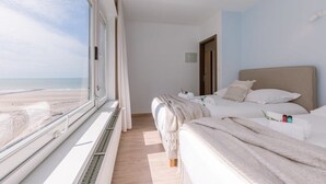 A hotel room with a large window overlooking the beach, two beds, a bedside table with toiletries, and a door leading to another room. - Waterfront retreat w/ Wifi & workspace (Middelkerke)