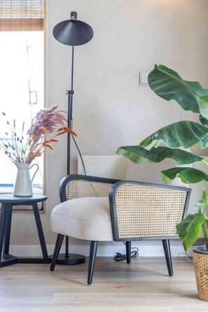 Un salon moderne avec un fauteuil en rotin, une lampe sur pied et une plante en pot.