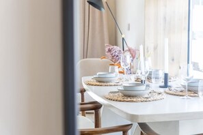 Une table à manger dressée avec des assiettes, des verres et des bougies, et un vase de fleurs en arrière-plan.