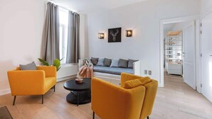Ein modernes Wohnzimmer mit zwei gelben Sesseln, einem grauen Sofa, einem runden Couchtisch und einem Wandbild mit einem Hirschgeweih.