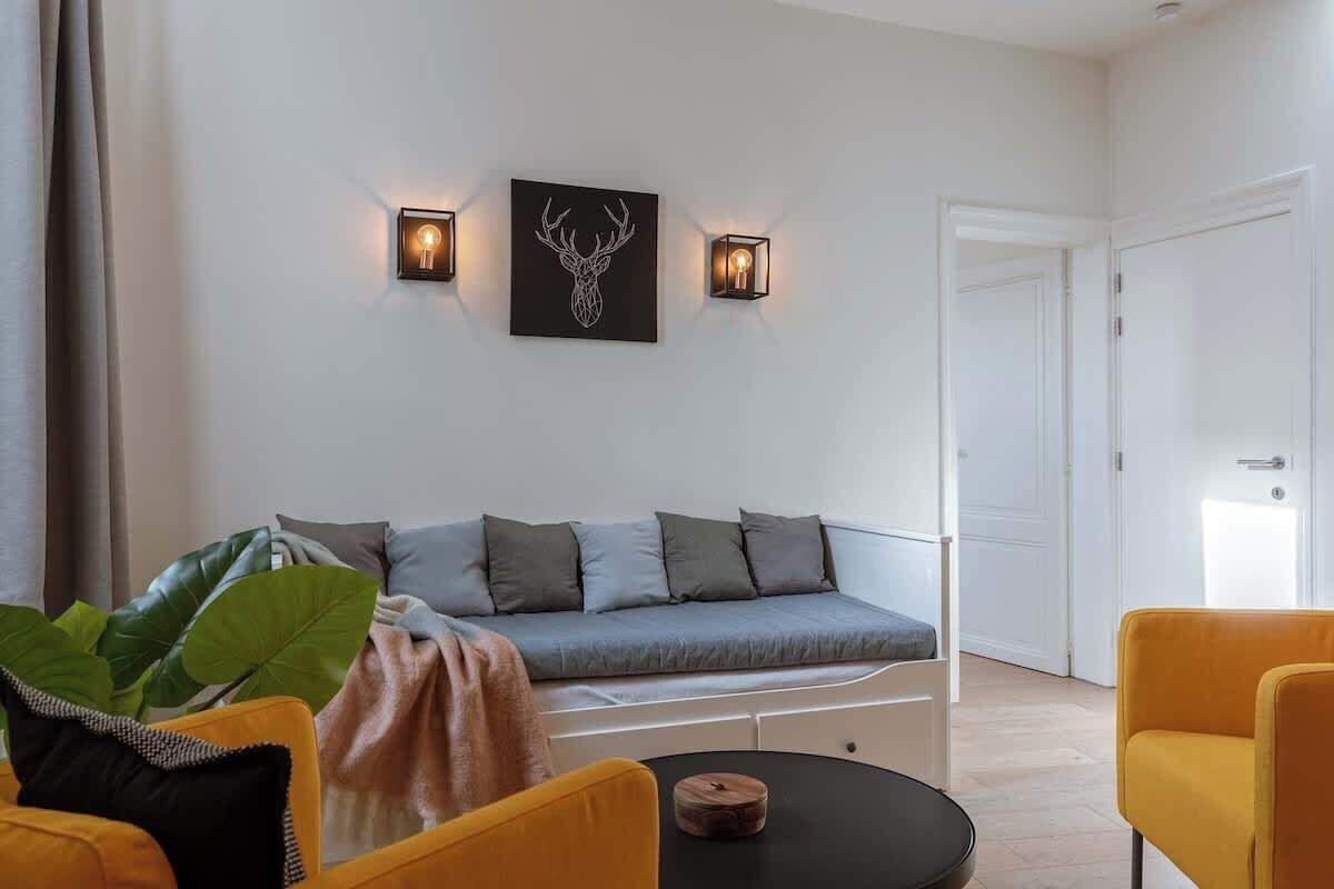 A modern living room with a grey sofa, yellow chairs, a round table, and wall-mounted lights.