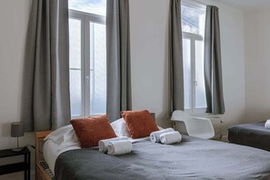 A hotel room with two beds, grey curtains, a white chair, and a window. - Historic Ghent Apartment, City Views, Walk to (Gent)