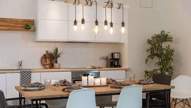 Eine moderne Küche mit weißen Schränken, einer Holz Arbeitsplatte und einem Essbereich mit zwei Stühlen und einem Tisch für zwei Personen.