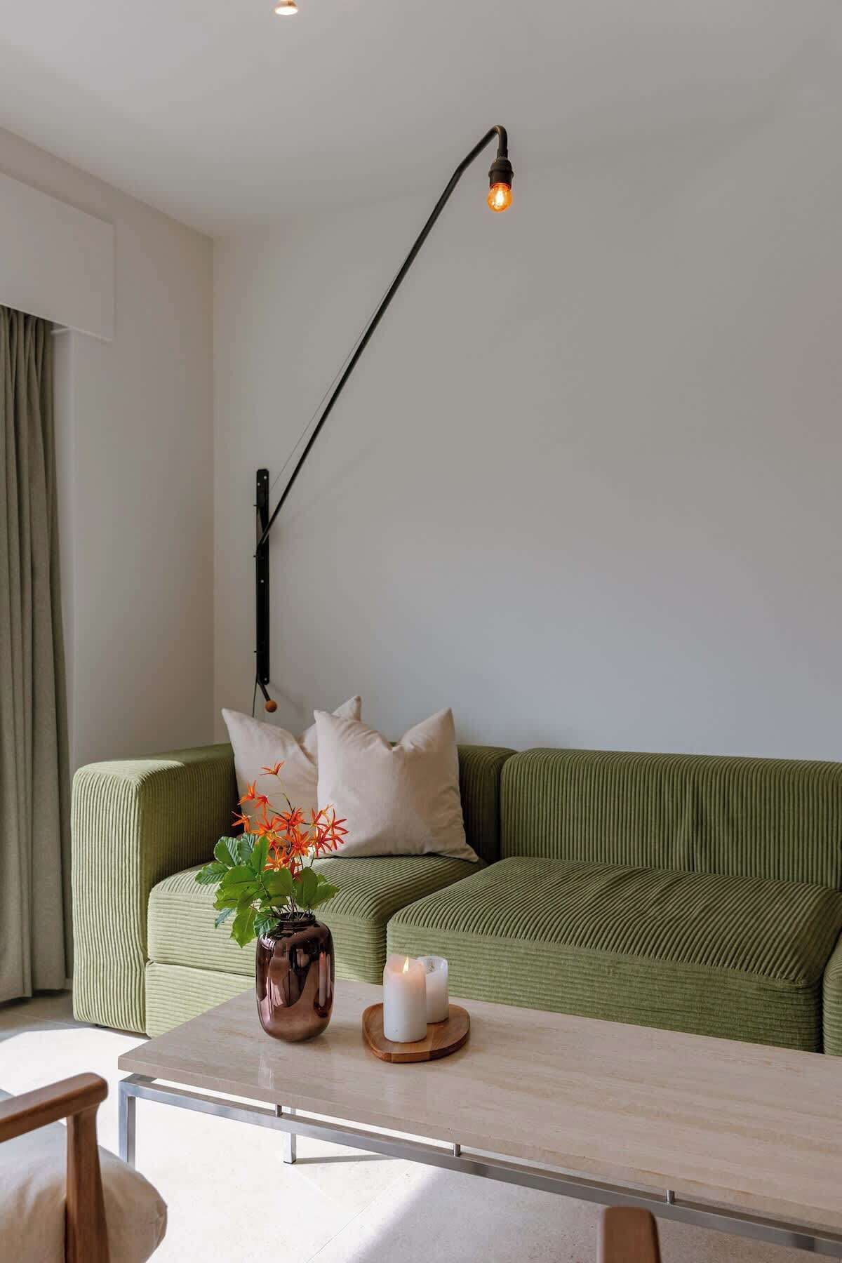 A modern living room with a green sofa, a coffee table, a vase with flowers, and a floor lamp.