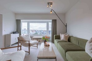 Een moderne woonkamer met een bank, fauteuil en salontafel, met uitzicht op de stad en een radiator.