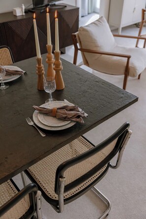 Een eettafel gedekt met borden, bestek en kaarsen, met stoelen eromheen.