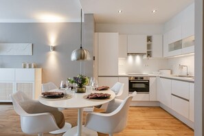 Een moderne keuken met witte kasten, een eethoek met witte stoelen en een hanglamp.