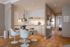Een moderne keuken met witte kasten, een eethoek met witte stoelen en een grote vloerlamp.