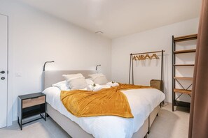 Un dormitorio con cama, mesita de noche, armario y perchero.