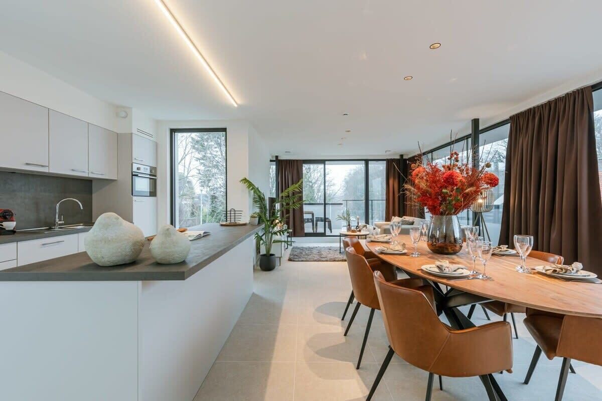 A modern kitchen with white cabinets, a large island, and a dining area with a wooden table and chairs.