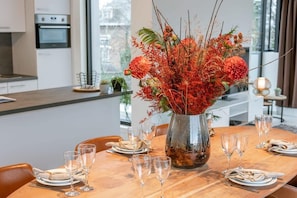 A dining table set with plates, glasses, and a centerpiece of red flowers. - Light-filled 2BR retreat w/ two terraces (Zedelgem)