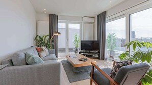 Un salon moderne avec un canapé, une table basse, un téléviseur et de grandes fenêtres.