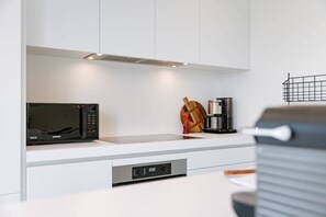 A modern kitchen with white cabinetry, a built-in microwave, a coffee maker, and a wooden cutting board.