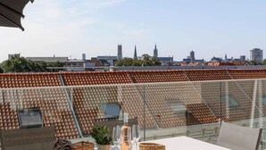 Une terrasse sur le toit, avec une table dressée pour deux personnes, une balustrade en verre et une vue sur la ville.