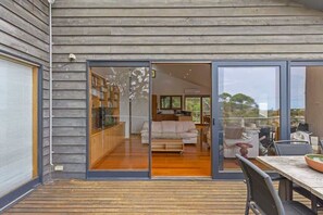 Una casa moderna con fachada de madera, puerta de vidrio que da a un espacio de estar con sofá, mesa de comedor y sillas.