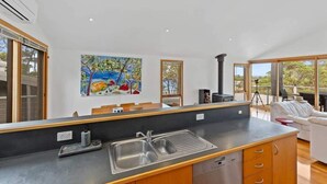 A modern kitchen with a large island, a dining area with a white sofa, and a painting on the wall. - Panorama at Rosedale (Rosedale)