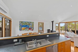 A modern kitchen with a large island, a dining area with a white sofa, and a painting on the wall. - Panorama at Rosedale (Rosedale)
