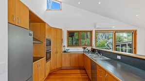 A modern kitchen with wooden cabinets, a stainless steel refrigerator, a built-in oven, and a large window providing a view of greenery. - Panorama at Rosedale (Rosedale)
