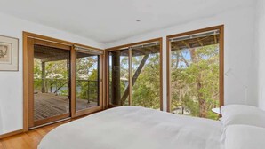 A bedroom with a large bed, sliding glass doors leading to a deck, and a view of trees and a body of water. - Panorama at Rosedale (Rosedale)