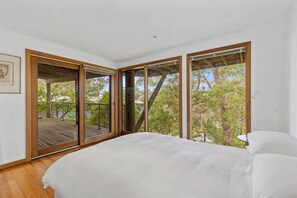 A bedroom with a large bed, sliding glass doors leading to a deck, and a view of trees and a body of water. - Panorama at Rosedale (Rosedale)