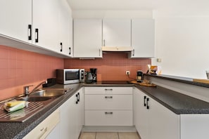 A kitchen with white cabinets, a microwave, a coffee maker, and a sink. - Beachfront Patio Apt in Koksijde w/ Natural Light (Koksijde)