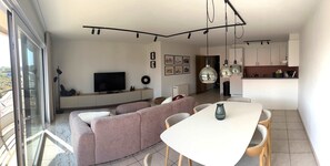 A modern living room with a sofa, TV, dining table, and kitchen area. - Coastal retreat near Beach at Koksijde (Koksijde)