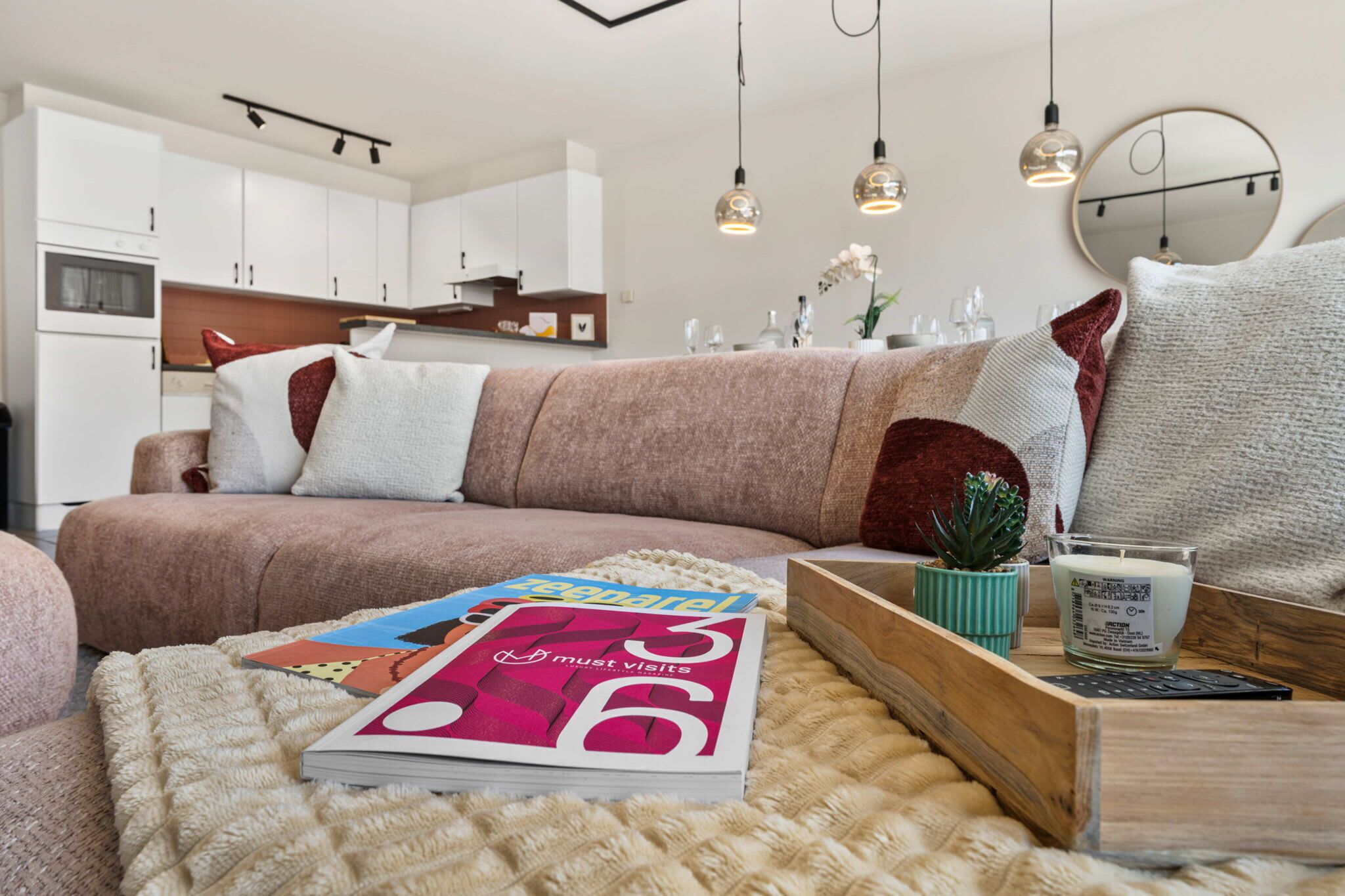 A modern living room with a sofa, a magazine, a small plant, and a candle on a wooden side table.
