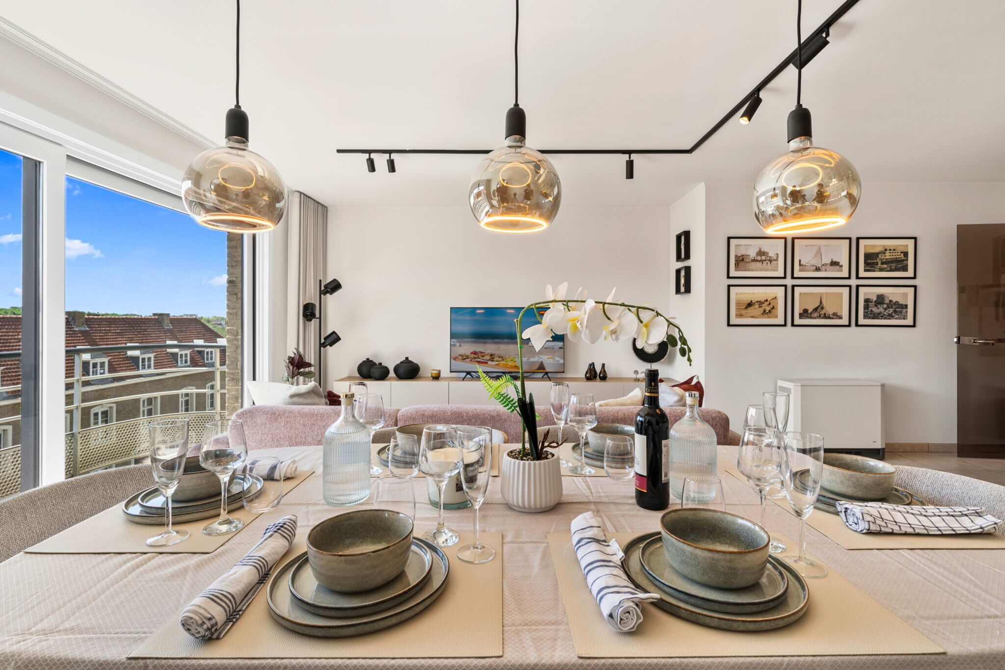 Un espace repas avec une table dressée pour quatre personnes, une vue sur le paysage urbain grâce à de grandes fenêtres et un aménagement intérieur moderne.